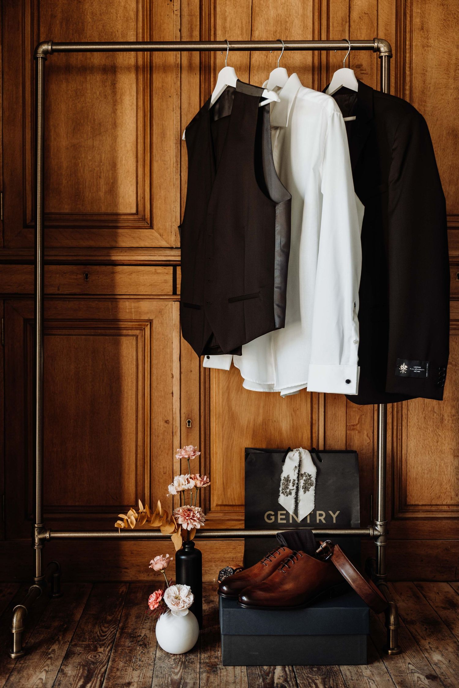 Gentry menswear suit, white dress shirt, and brown leather shoes displayed on industrial pipe clothing rack.