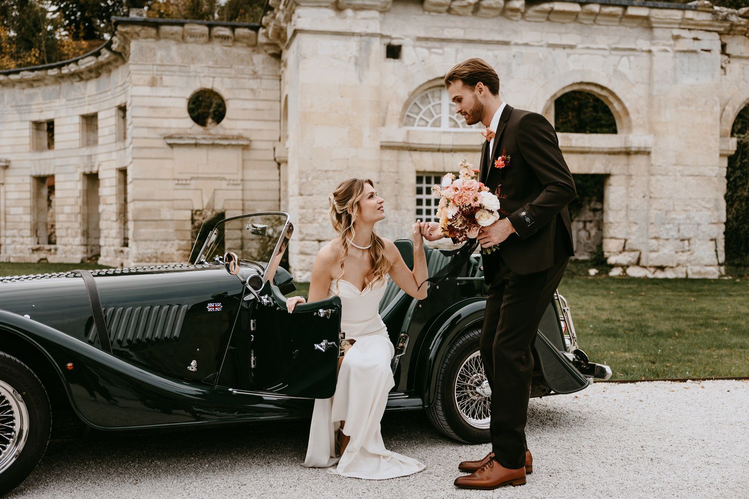 Bride and groom sharing a romantic moment beside a vintage convertible car at an elegant outdoor wedding venue.