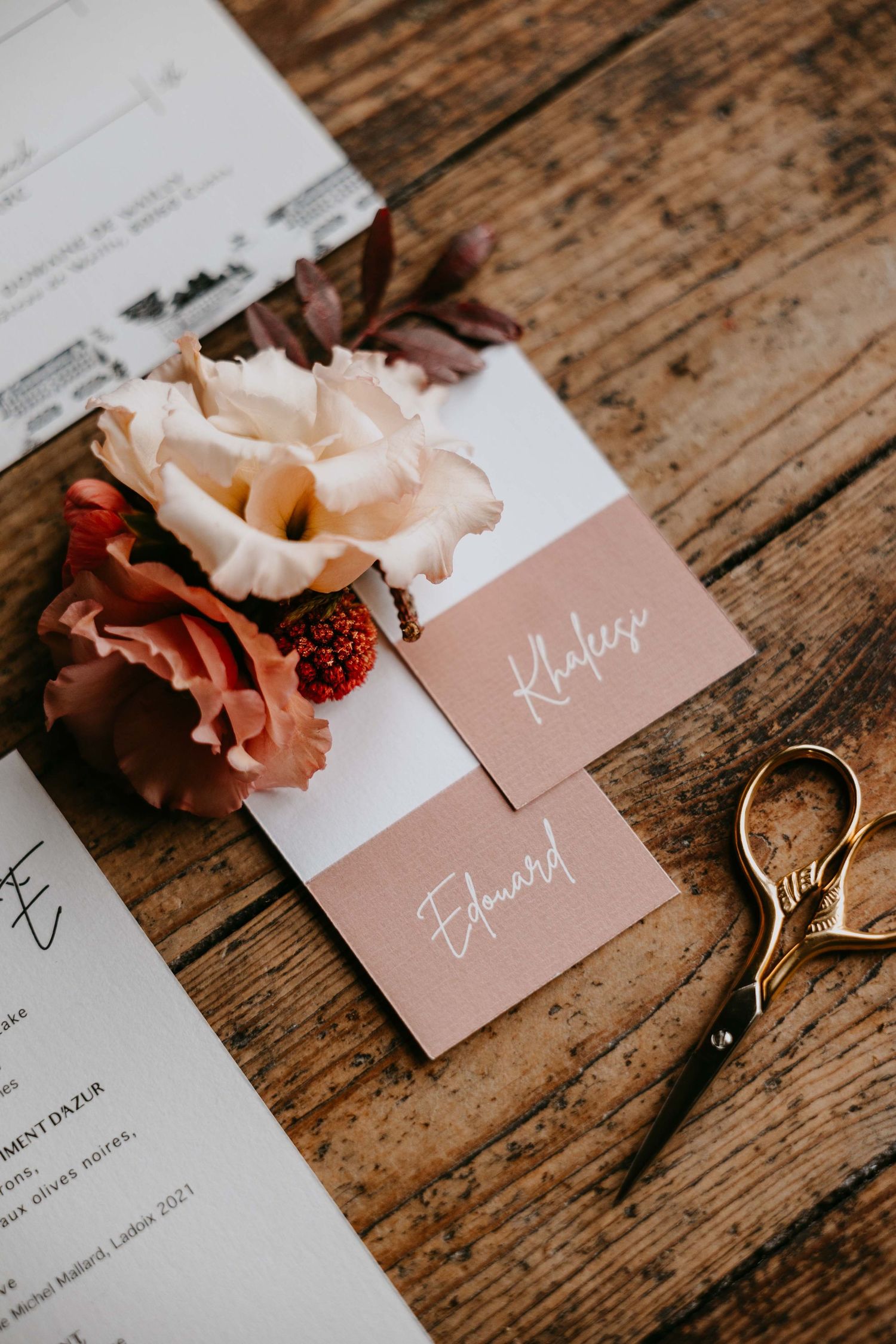 Elegant wedding place cards with calligraphy on rustic wood table, adorned with dried florals and gold scissors.
