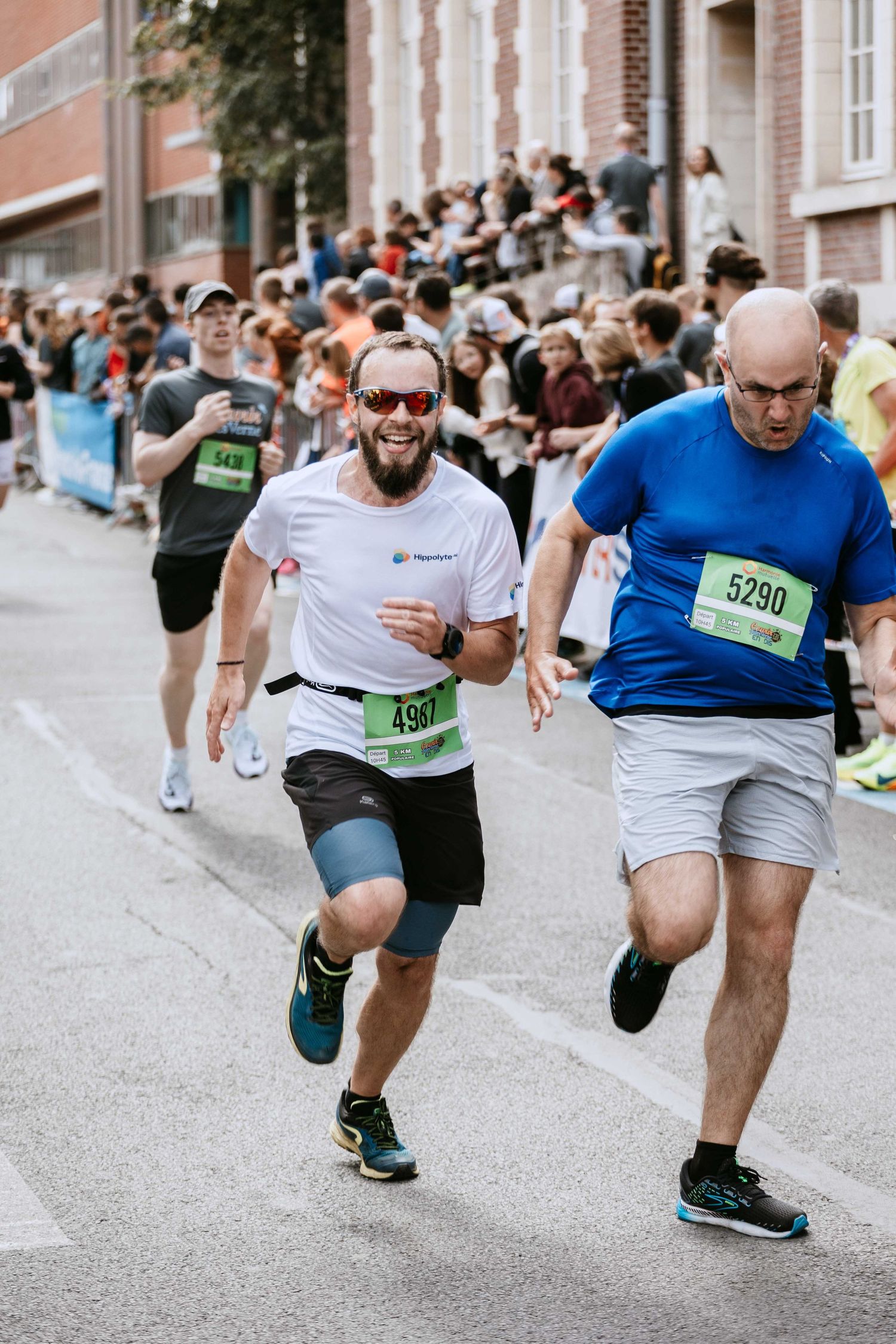 Two male runners wearing race bibs sprinting toward the finish line of an outdoor city road race.