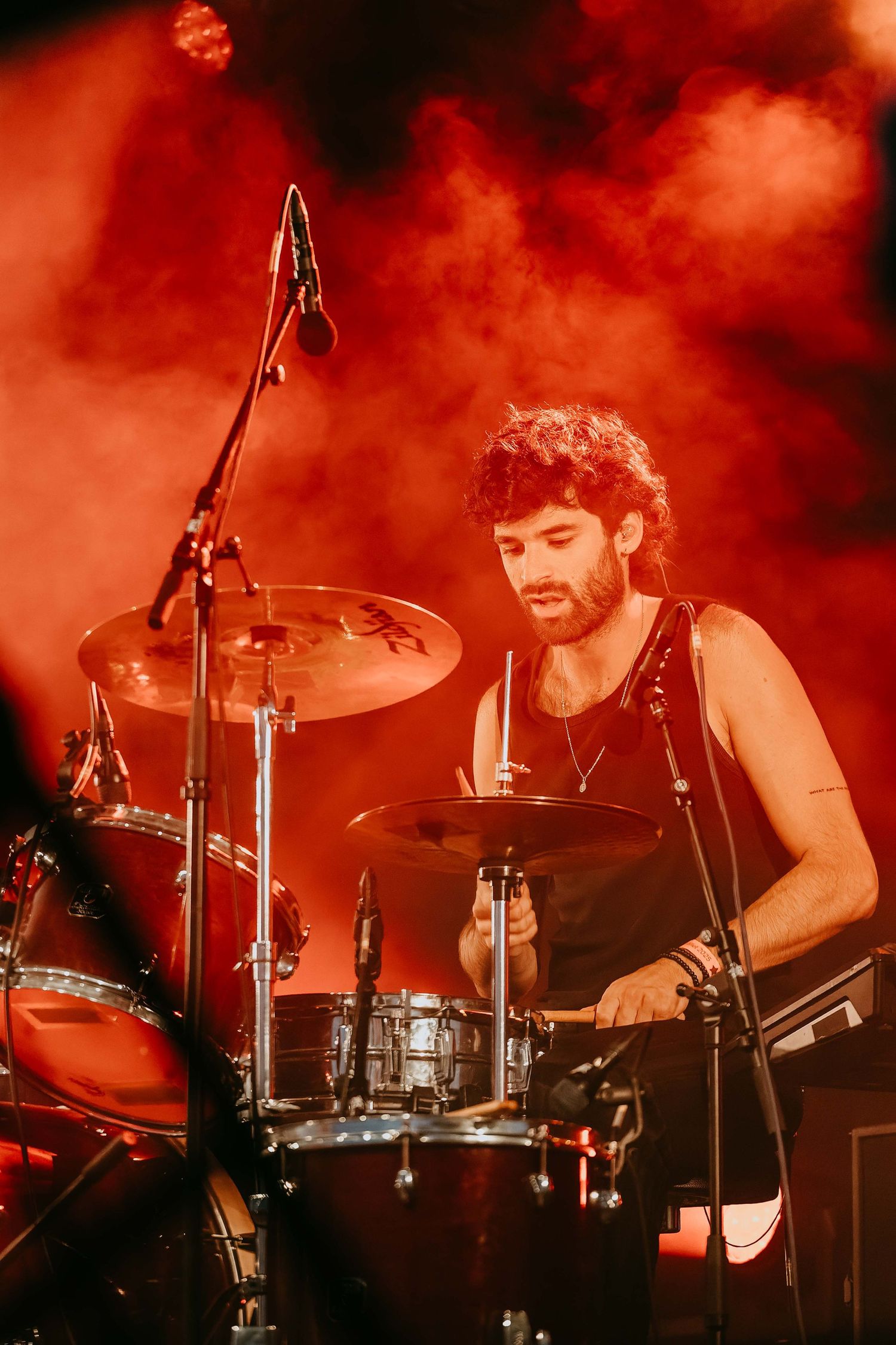 Male drummer performing on stage surrounded by dramatic red smoke at a live concert.