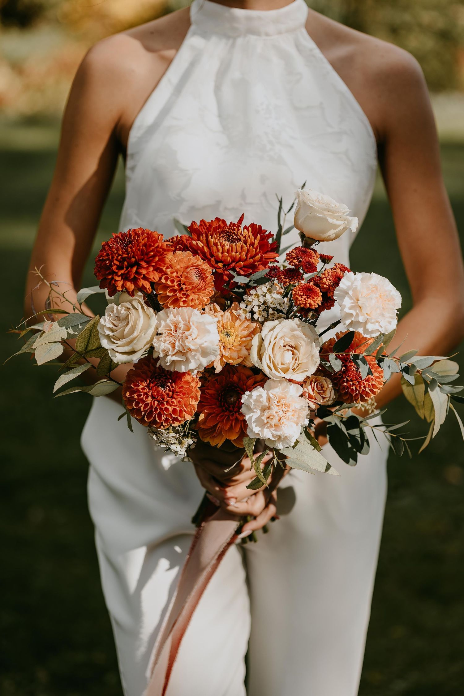 Close-up of a fall bridal bouquet with orange chrysanthemums and cream roses held by a bride.