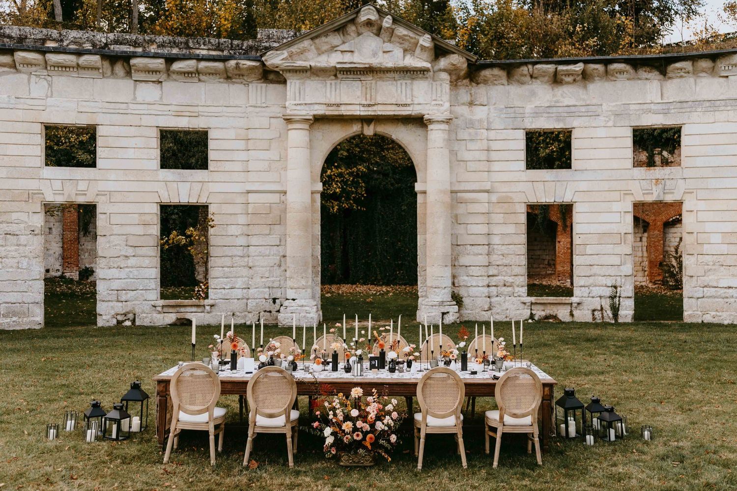 Elegant outdoor wedding reception table set before a rustic stone chateau with floral centerpieces and candles.