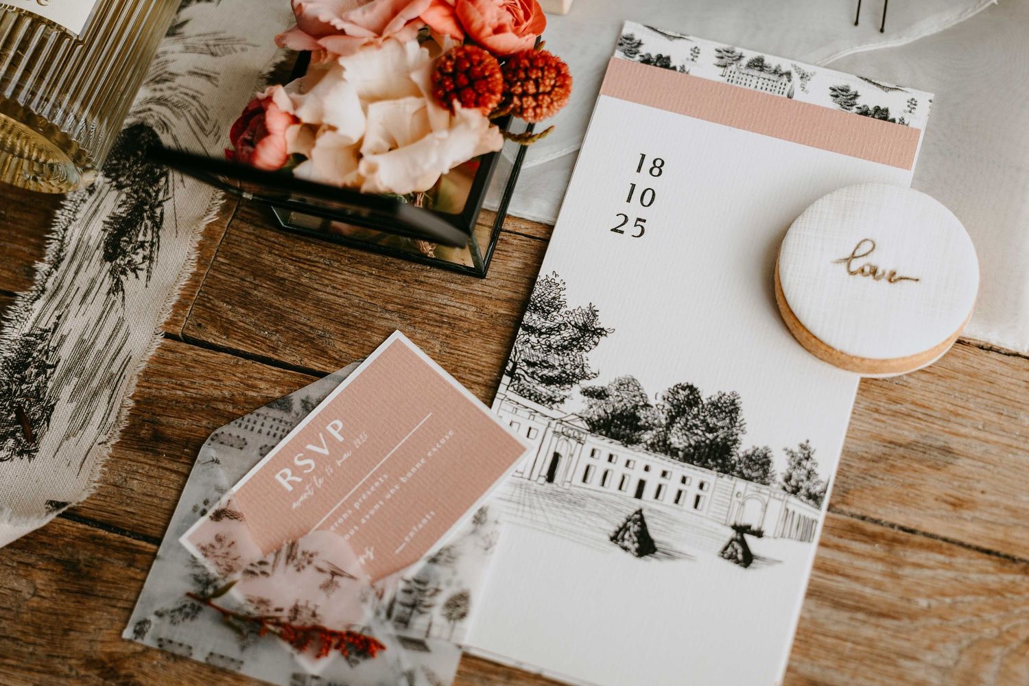 Elegant wedding stationery flat lay with invitation suite, RSVP card, and floral arrangement on rustic wood table.