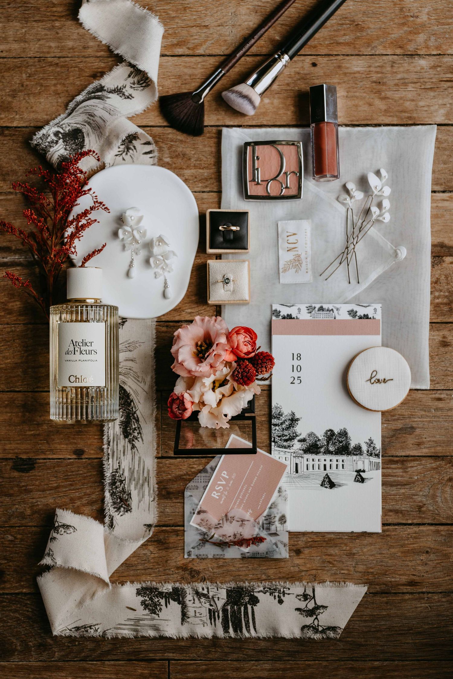 Flat lay of wedding details including Dior makeup, Chloe perfume, flowers, and stationery.