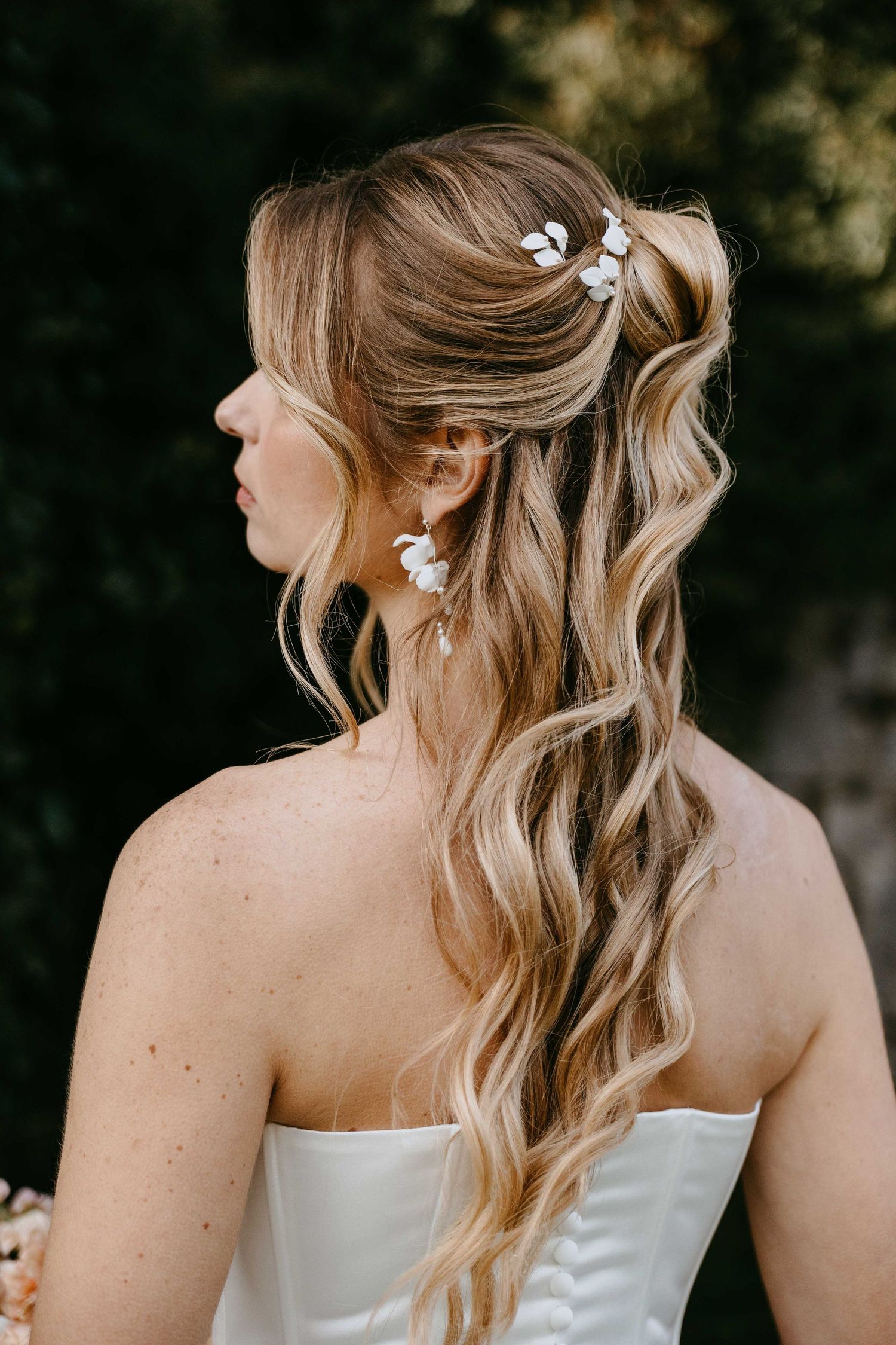Bride with wavy blonde half-up hairstyle adorned with delicate white floral hair pins and matching drop earrings.
