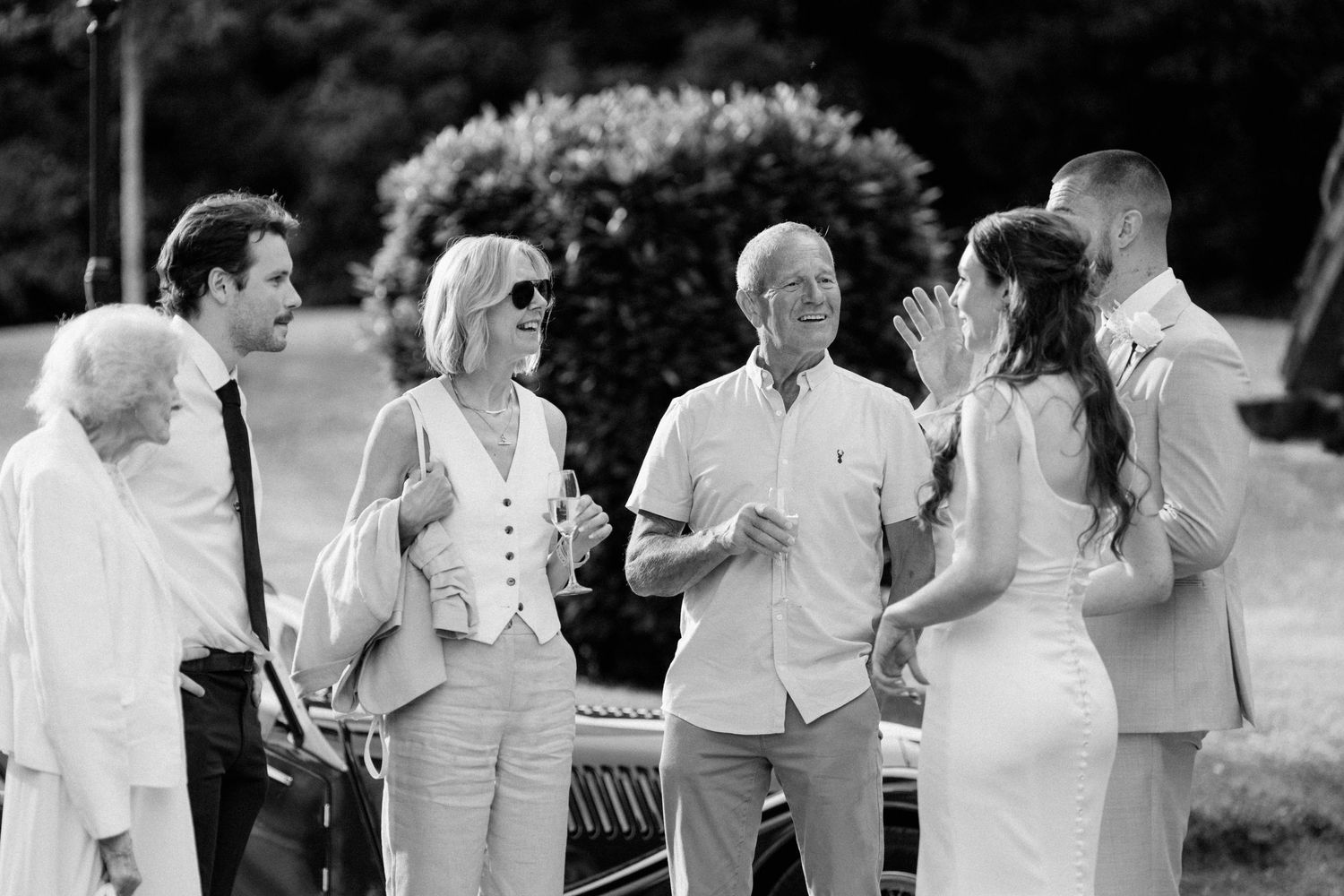 Bride and groom greeting family members outdoors in black and white wedding photo.