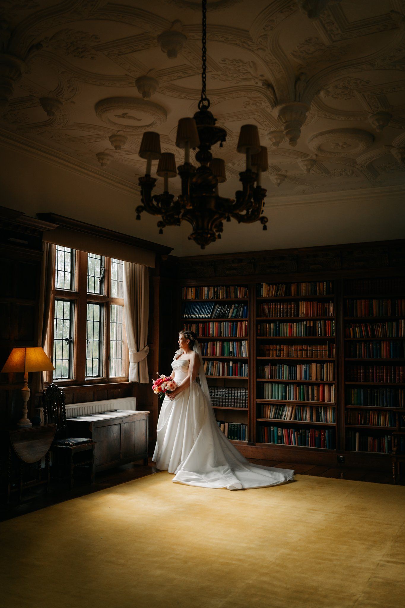Bride standing by the tall leaded windows in the library at Brinsop Court, Herefordshire