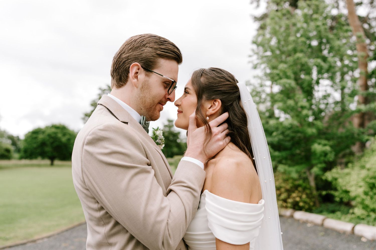 Groom tenderly holds brides face as they share an intimate moment outdoors on their wedding day.