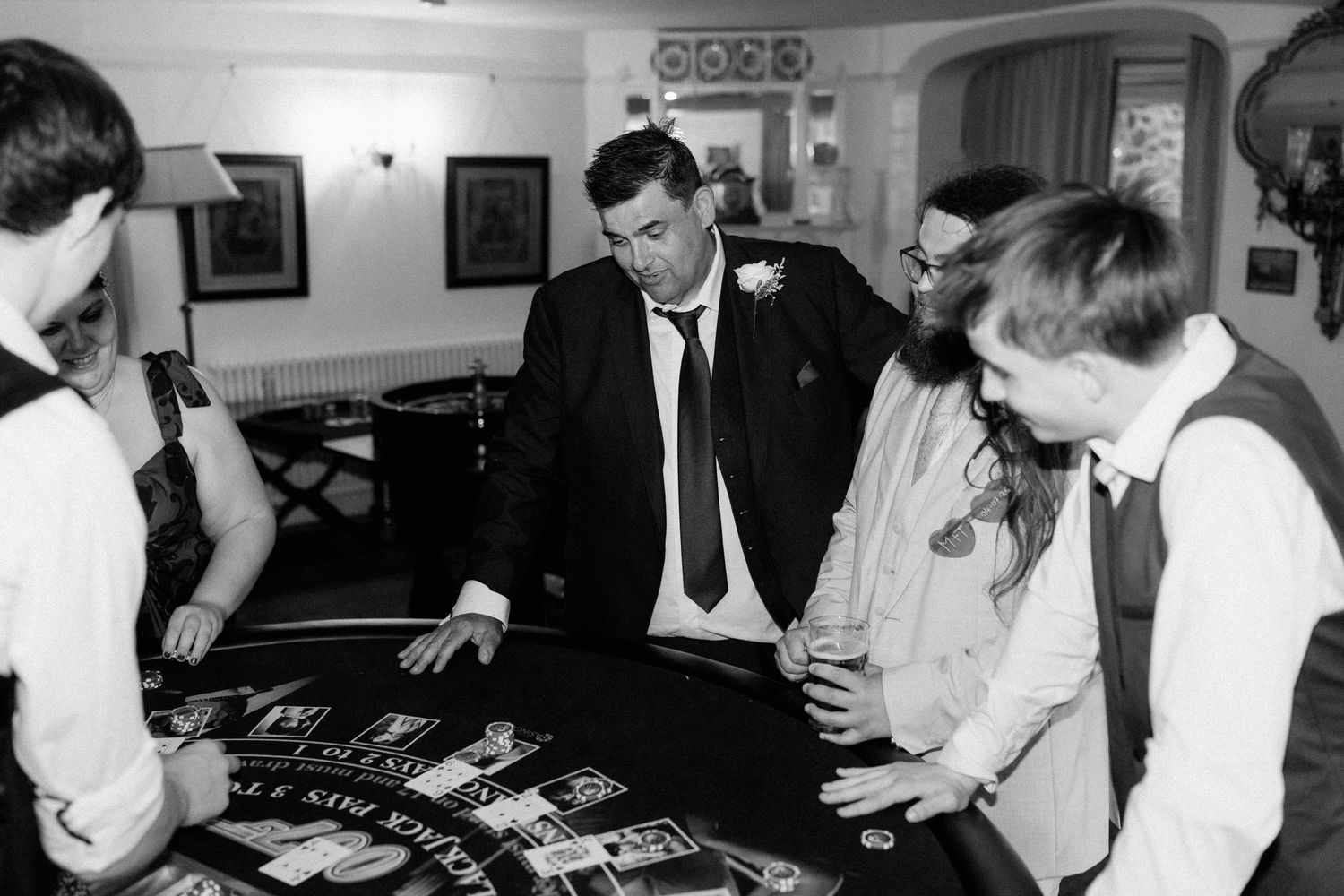 Black and white photo of men playing blackjack at a casino table during a formal event.