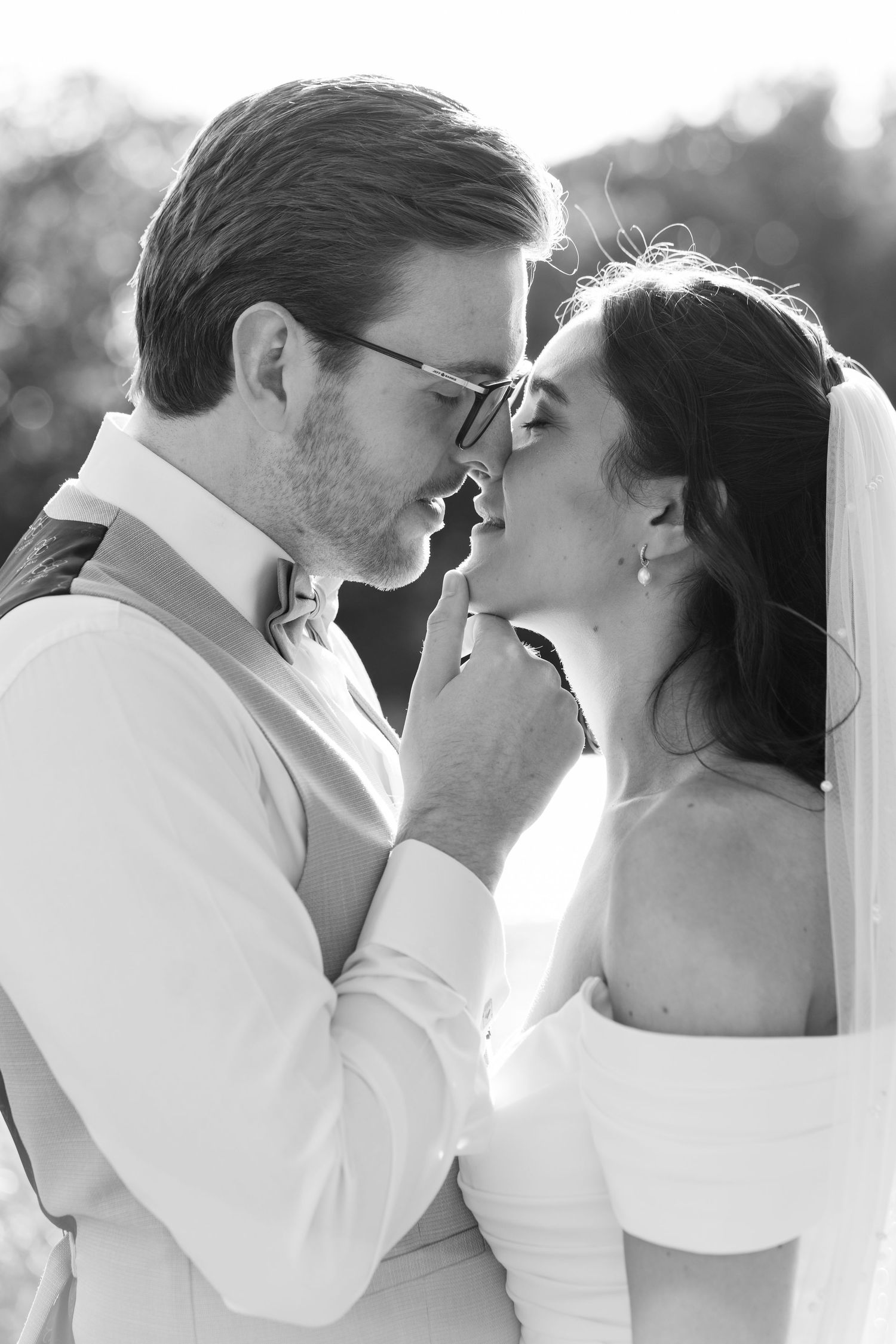 Black and white photo of a bride and groom sharing an intimate moment, nearly kissing on their wedding day.