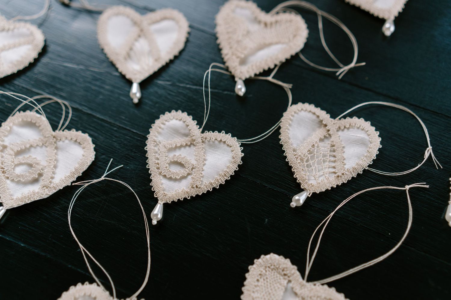 Decorative lace heart ornaments with pearl details arranged on dark wooden surface.