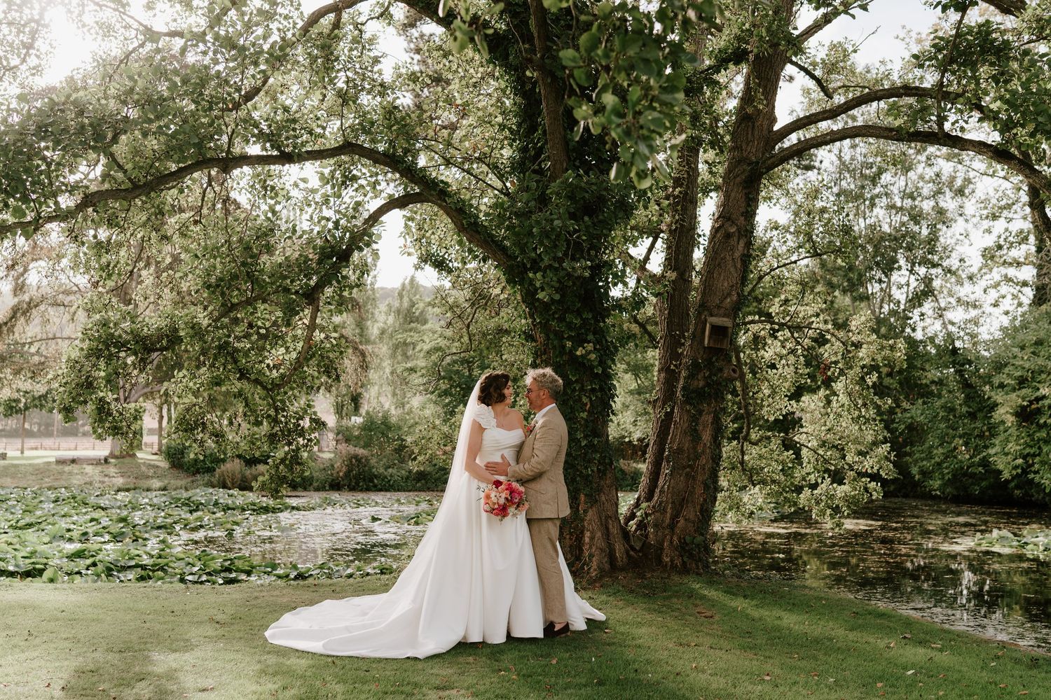 Bride and groom under an old tree beside the lily pond, Herefordshire wedding