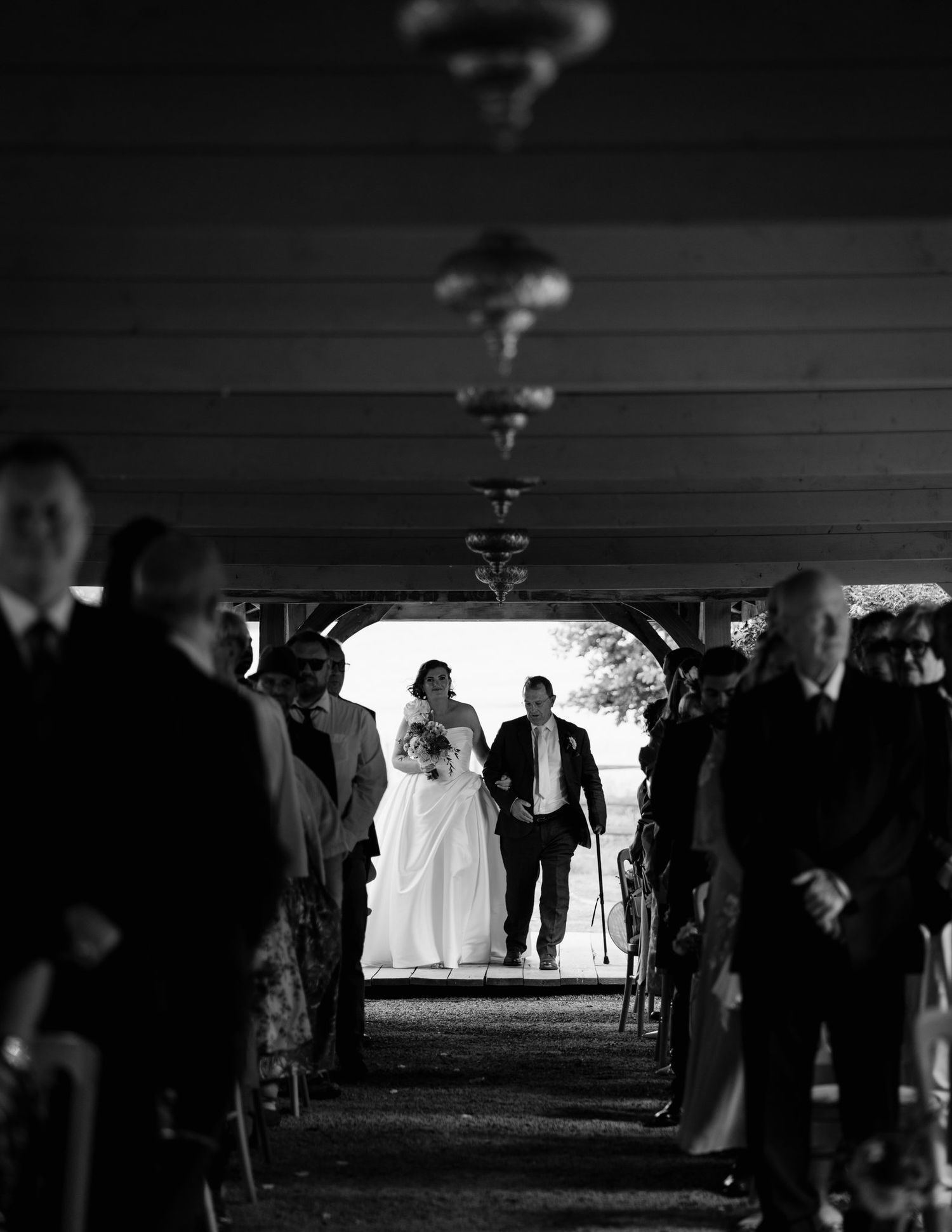 Black and white photo of a bride and her dad walking down the aisle at an outdoor wedding ceremony at Brinsop Court
