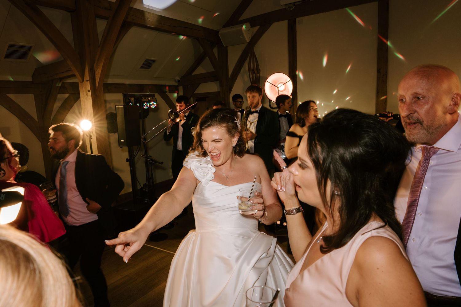 Bride dancing joyfully with guests at a wedding reception in a warmly lit venue.