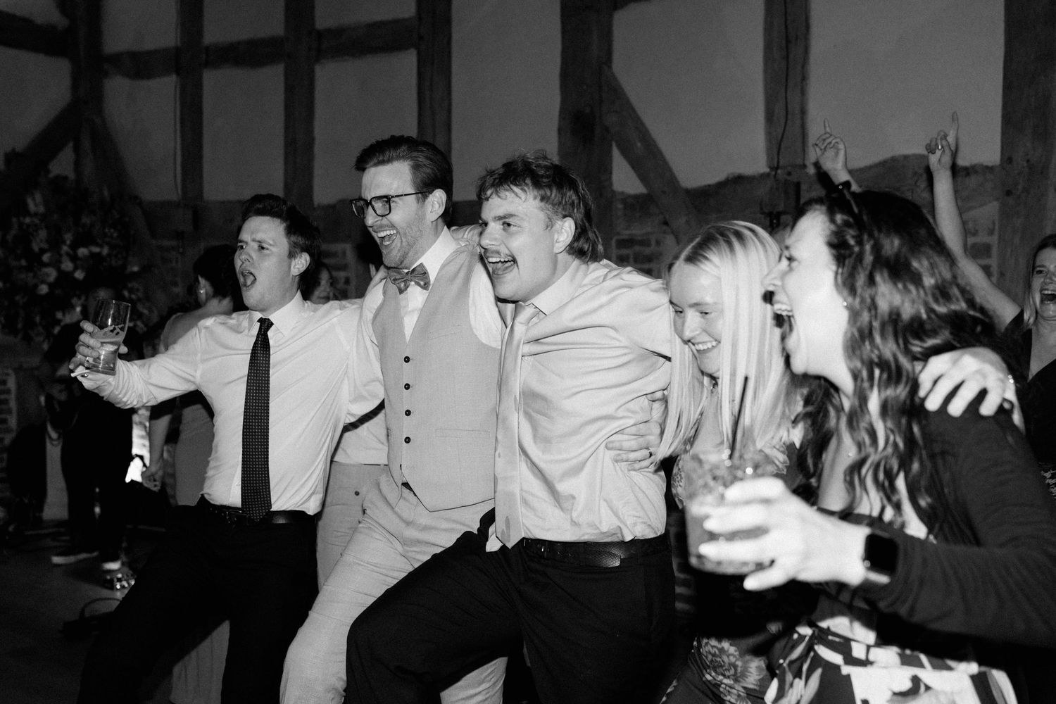 Group of wedding guests dancing and celebrating together in a rustic barn venue in black and white.