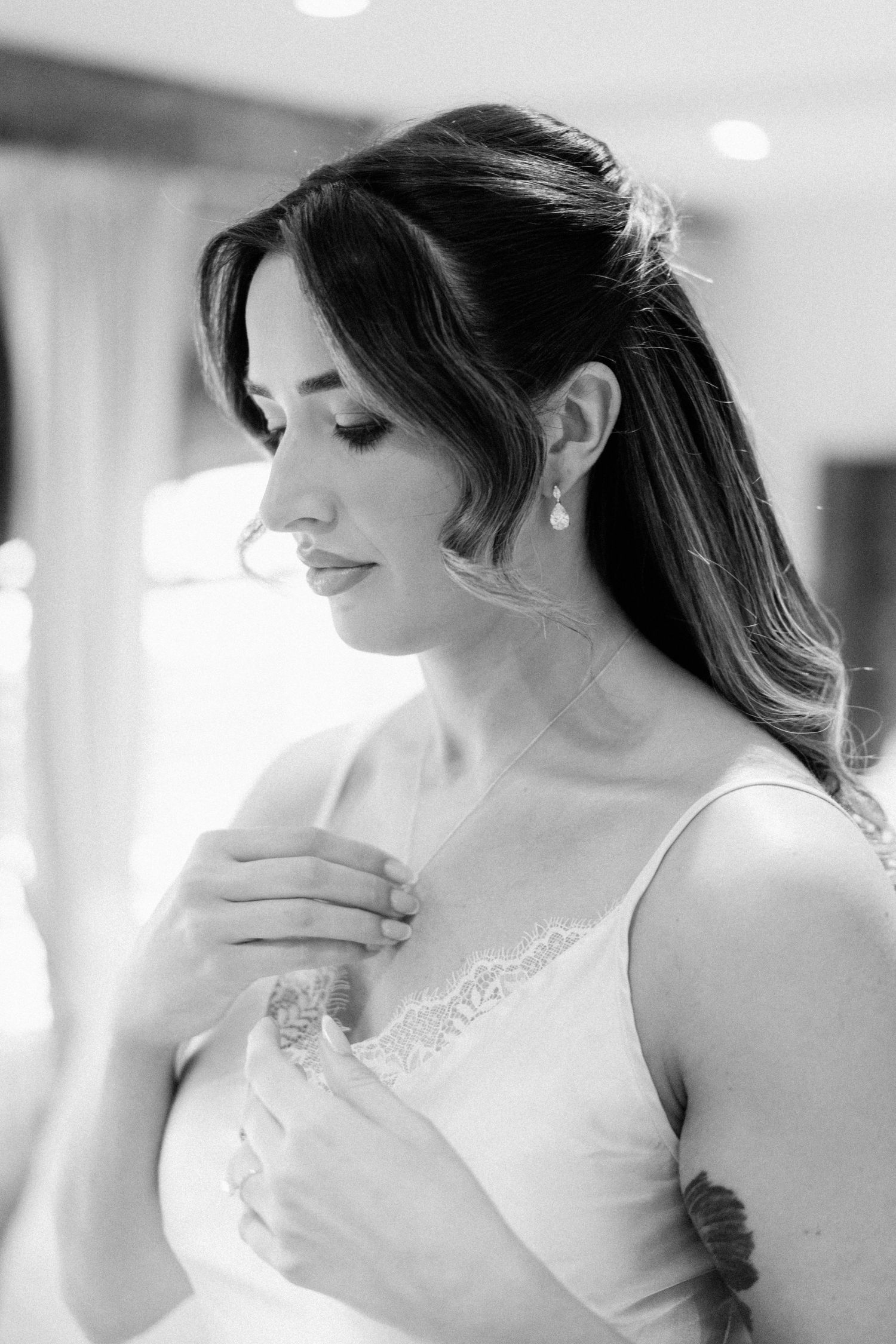 Black and white portrait of a bride in a lace wedding dress, looking down elegantly with pearl earrings.