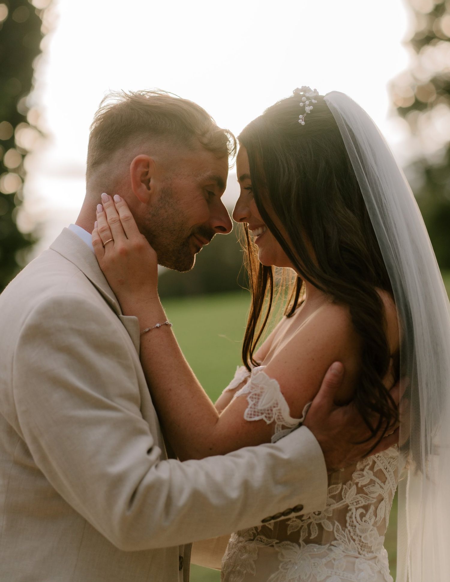 A bride and groom share an intimate moment at golden hour, touching foreheads outdoors at their wedding.