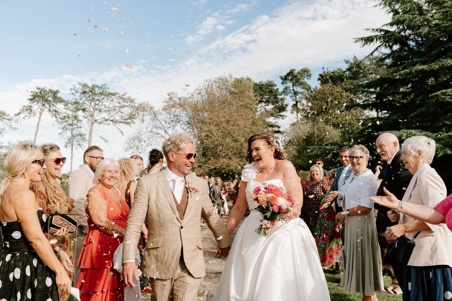 Guests throwing confetti over the newlyweds under a blue September sky at Brinsop Court, Herefordshire