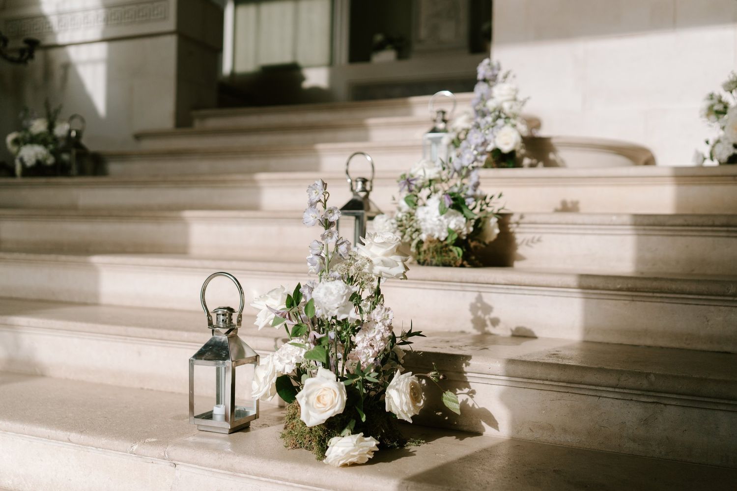 White floral arrangements and a silver lantern decorating marble church steps for an elegant wedding ceremony.