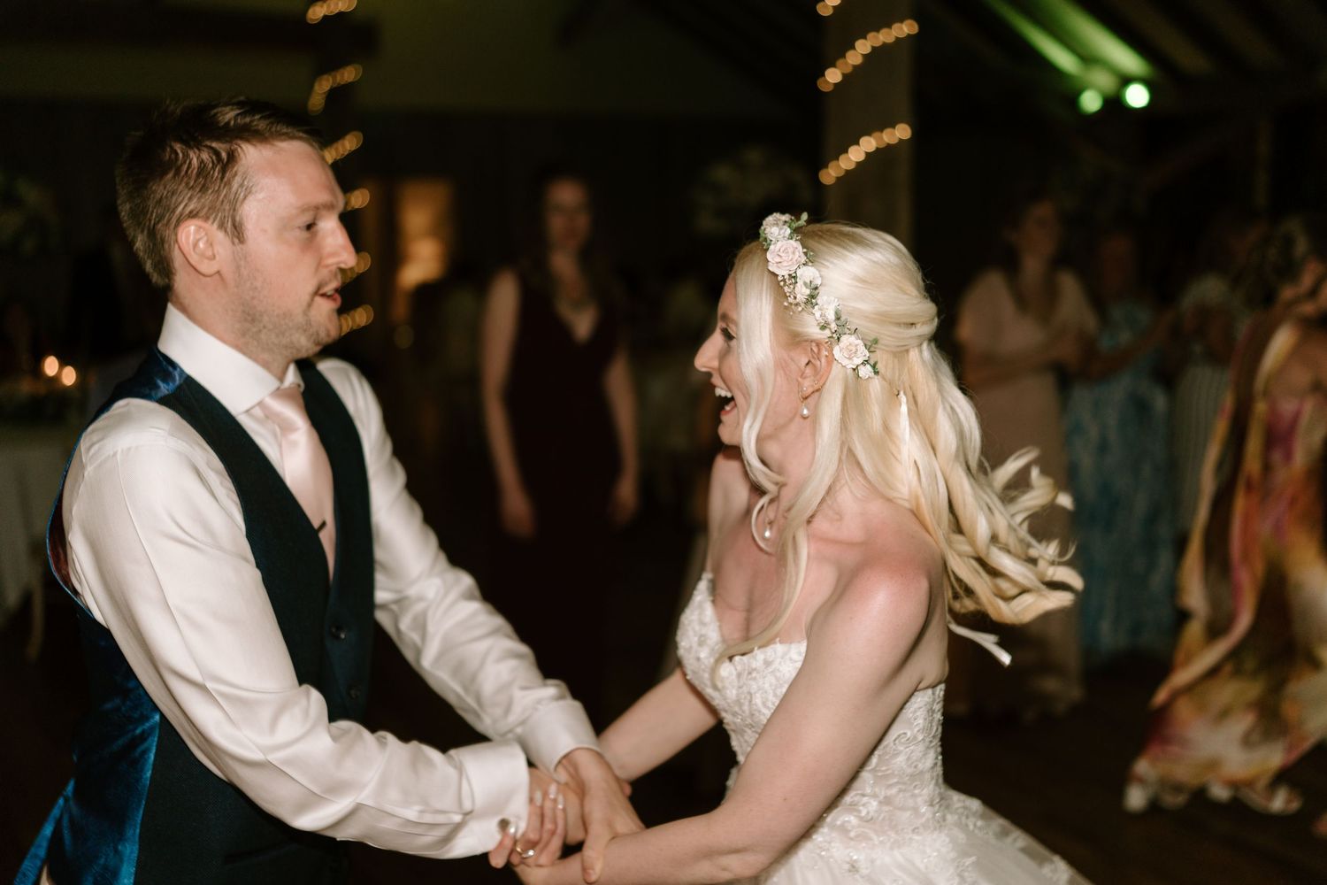 Bride and groom share a joyful first dance, holding hands and laughing at their wedding reception.