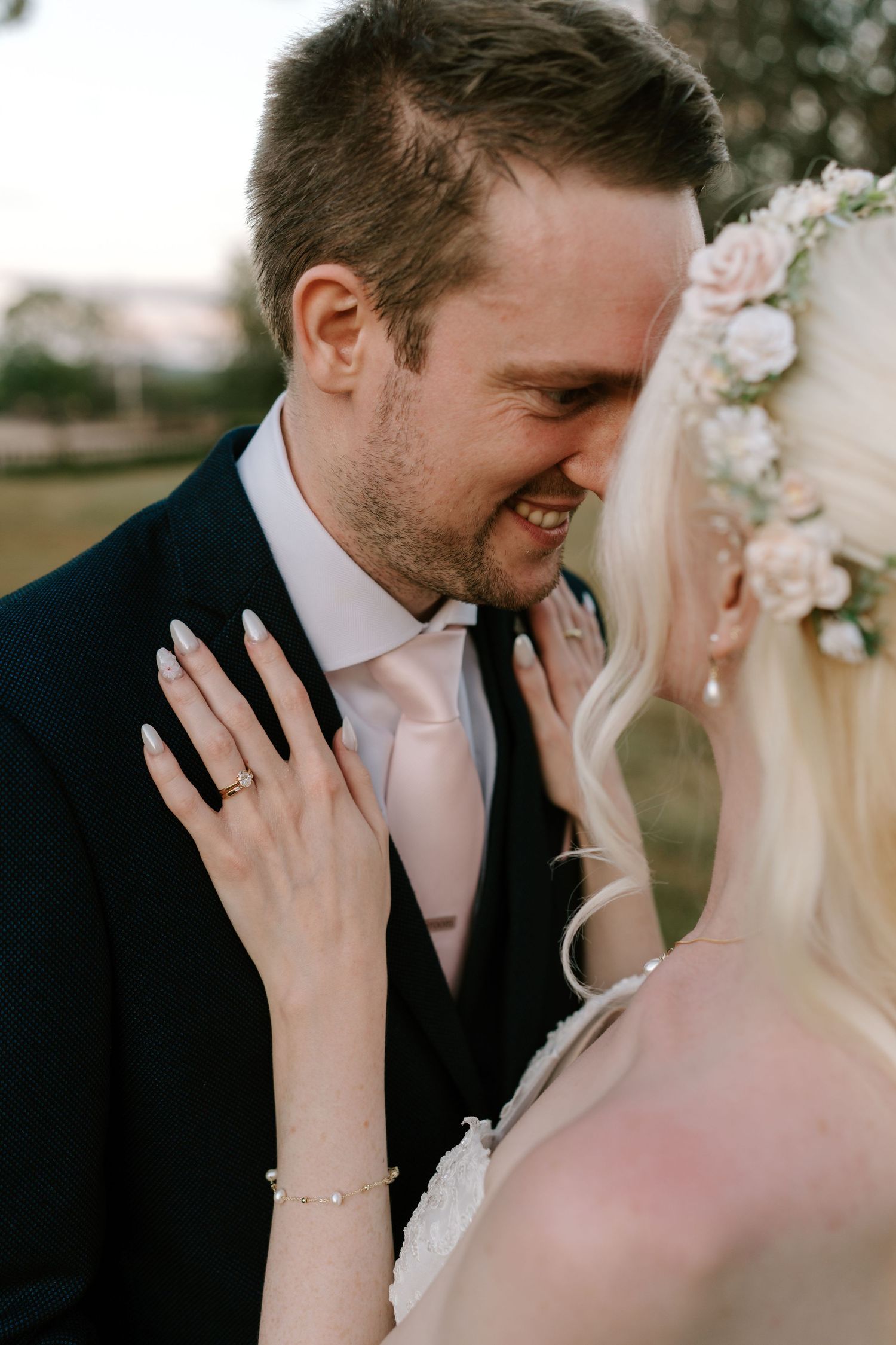 Bride and groom sharing a romantic moment, bride wearing floral crown and wedding ring, groom in navy suit with pink tie.