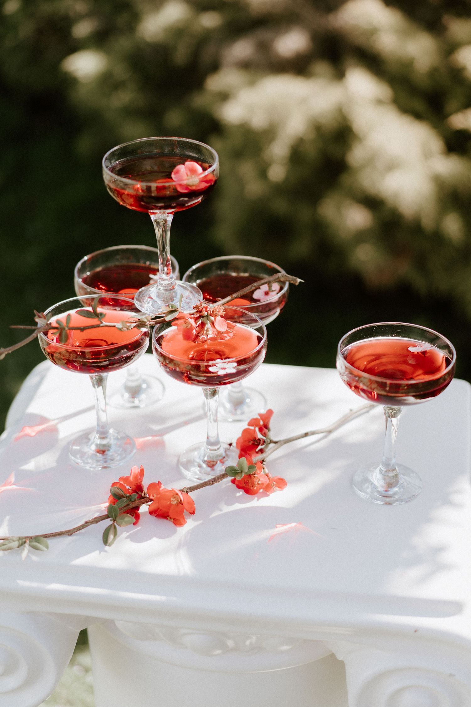 Elegant pyramid of red wine coupes garnished with flowers on a white table outdoors.