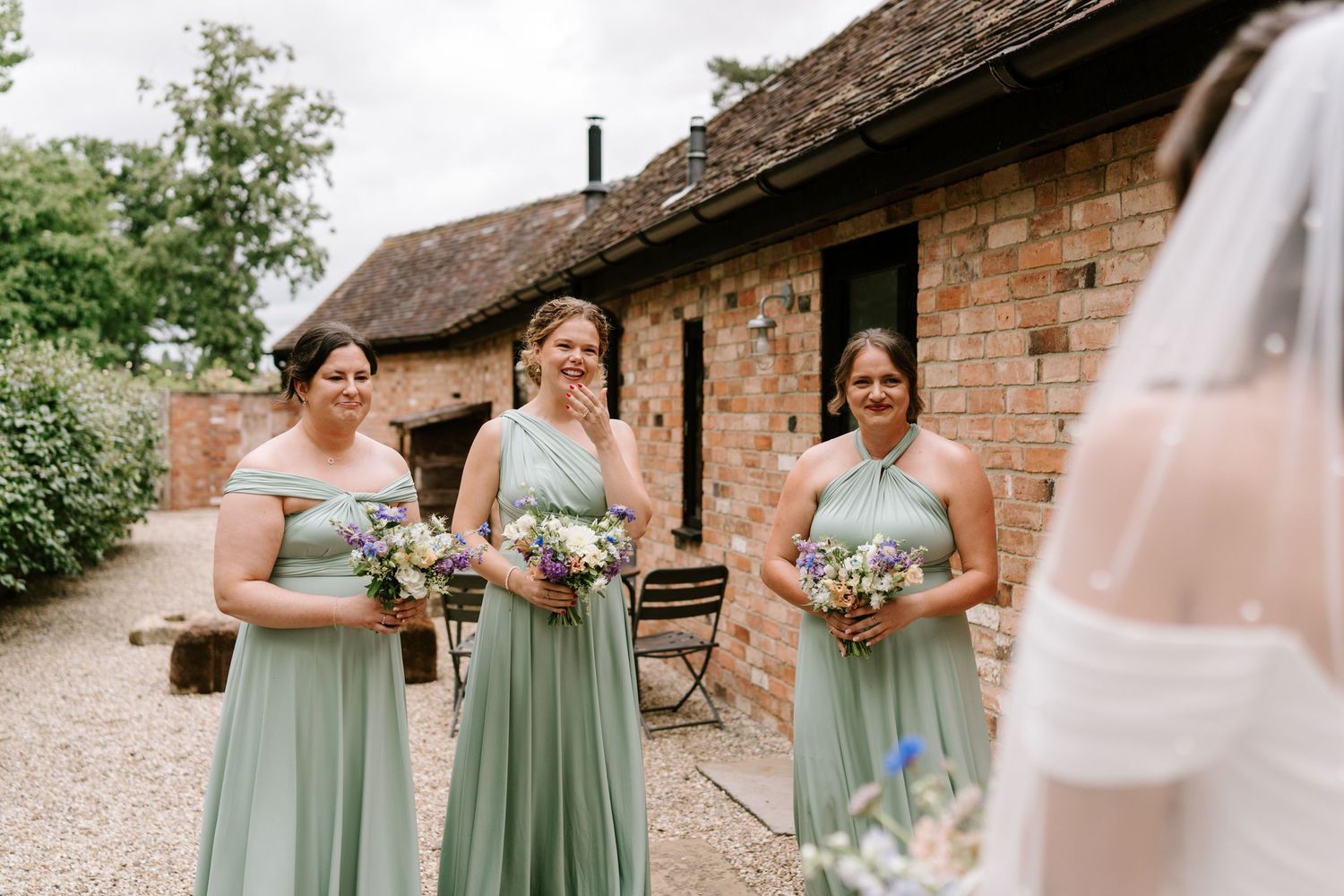Bridesmaids in mint green dresses laughing and reacting emotionally as bride reveals her wedding look.
