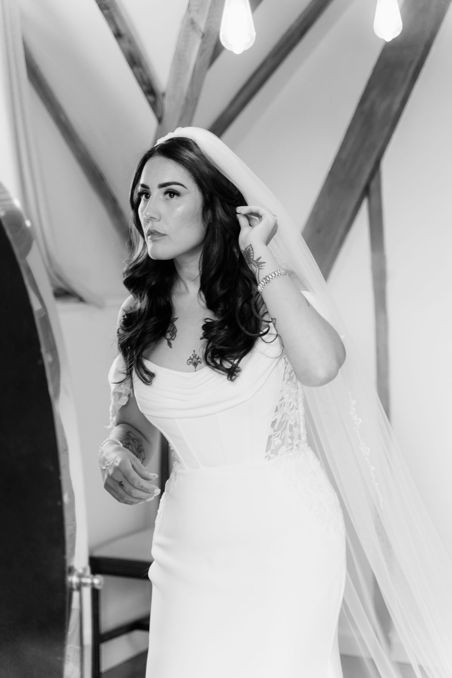 Black and white photo of a bride in a white gown and veil, posing elegantly with tattoos visible.