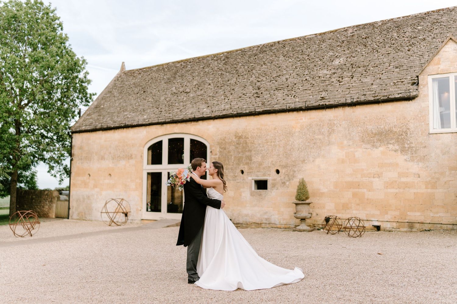 Bride and groom share a romantic dance outside a rustic stone barn venue on their wedding day.