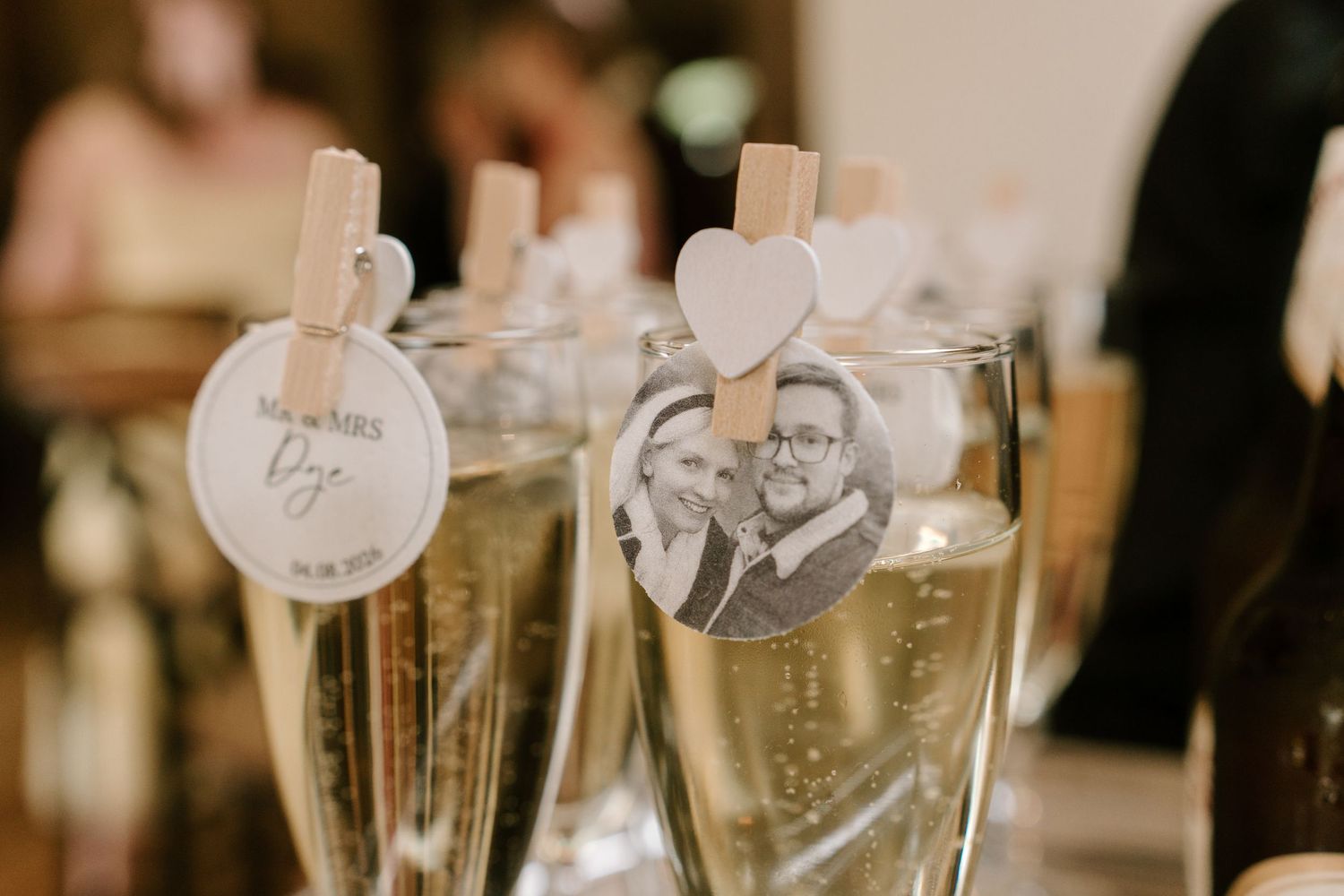 Wedding champagne flutes decorated with personalized photo tags and heart clothespins for a romantic celebration.