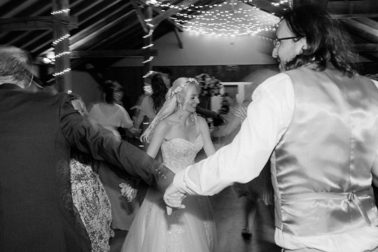 Bride and groom share a joyful first dance surrounded by guests at their wedding reception in black and white.
