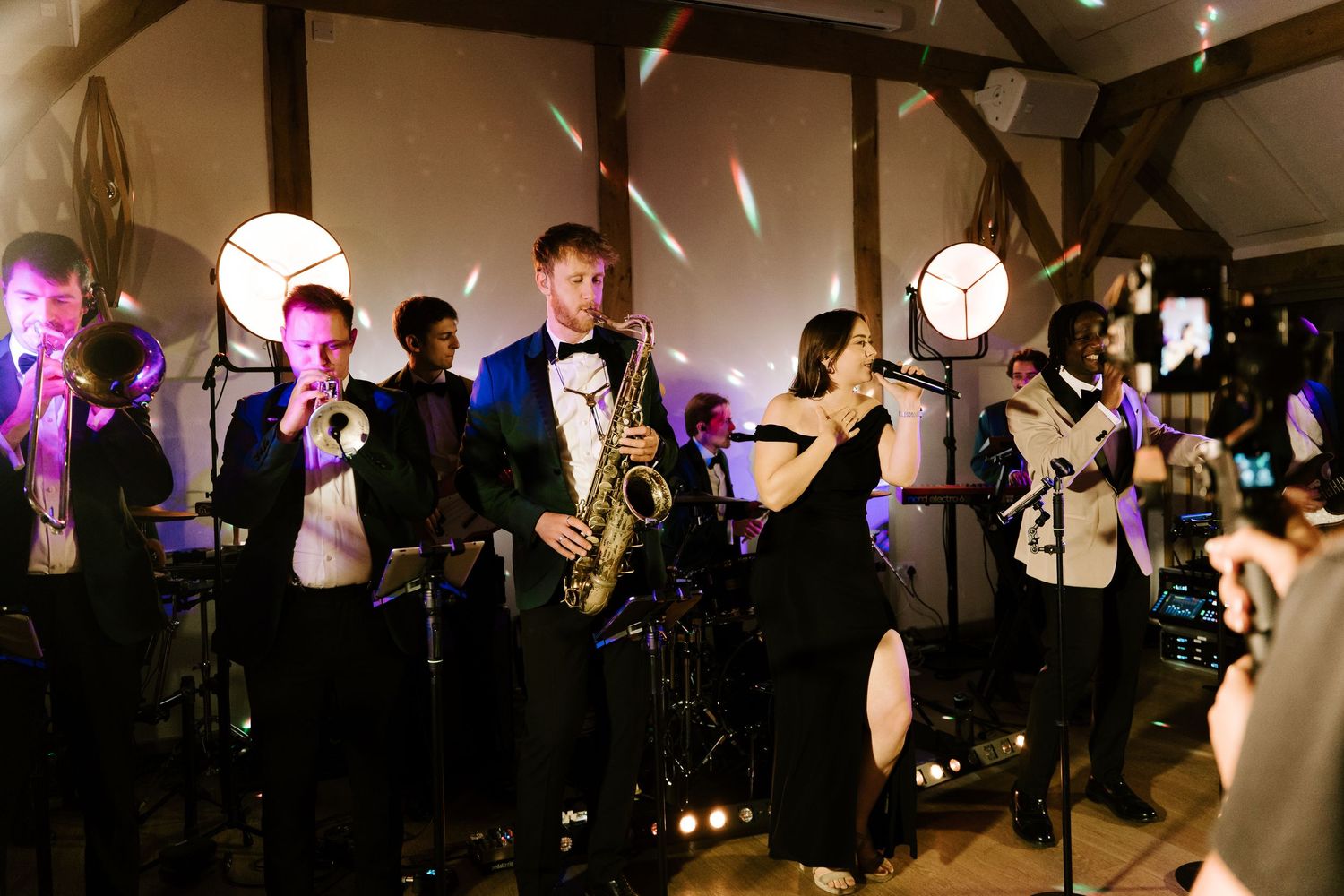 A live jazz band performs at an elegant wedding reception, featuring saxophone, trumpet players in formal black tie attire.