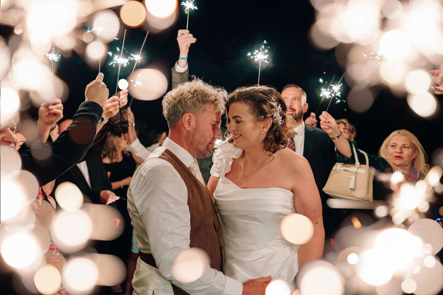 A bride and groom share a romantic moment surrounded by guests holding sparklers at their wedding reception.