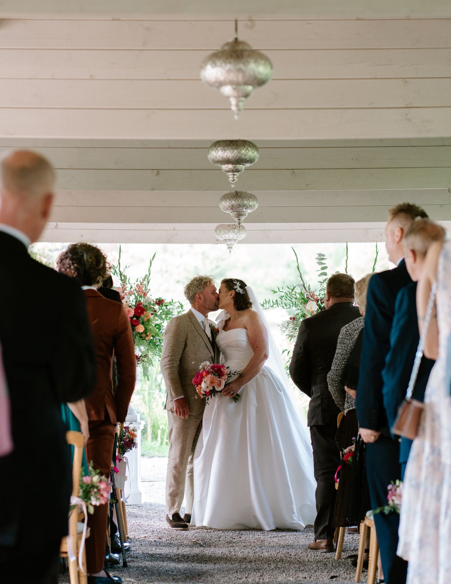 Bride and groom's first kiss in the Astley Pergola, surrounded by guests at Brinsop Court
