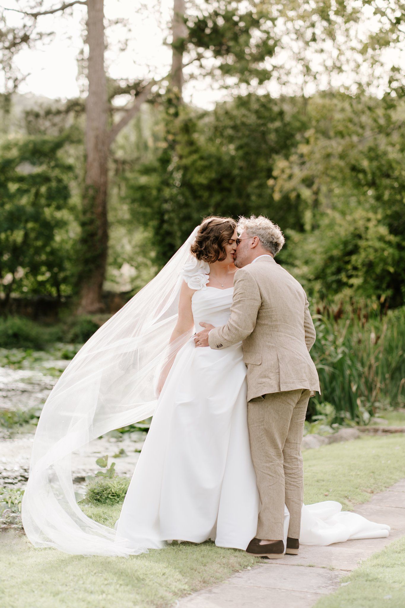 Bride's veil catching the breeze as the groom kisses her in the gardens at Brinsop Court