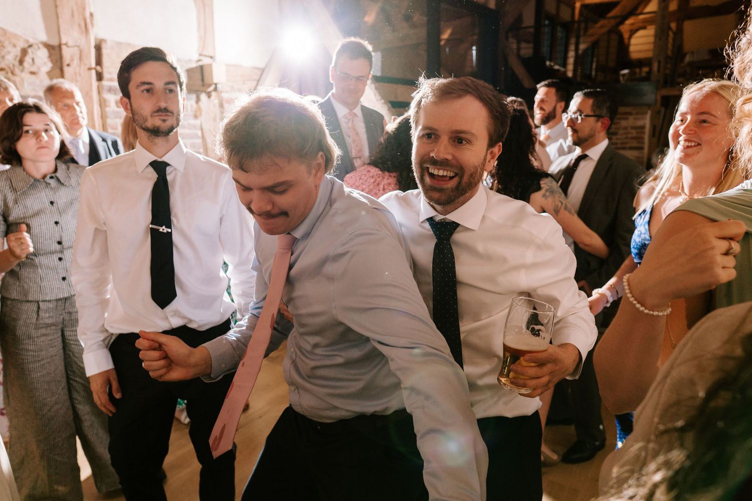 Guests dancing and celebrating joyfully at a wedding reception in a rustic venue.