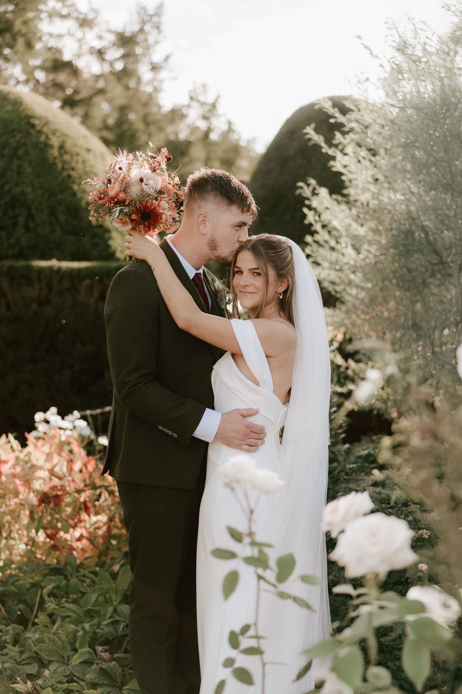 Bride and groom embrace in a lush garden at Birtsmorton Court, Worcestershire wedding venue