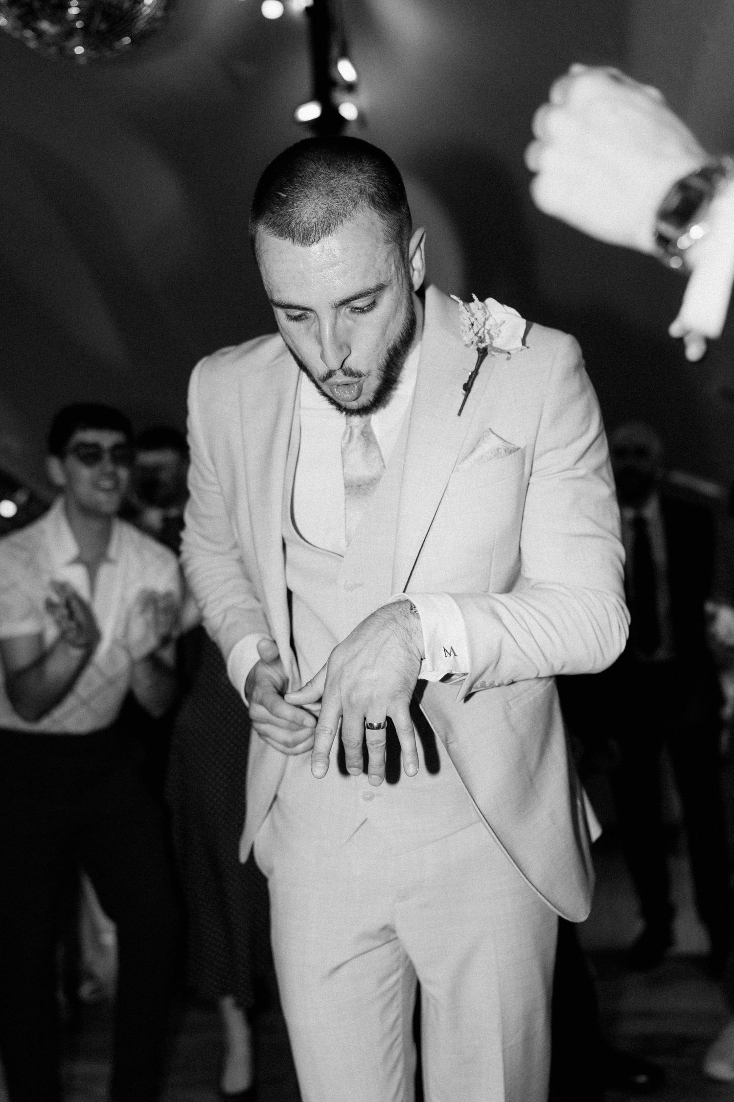 Groom in light suit with boutonniere dances at wedding reception in black and white photo.