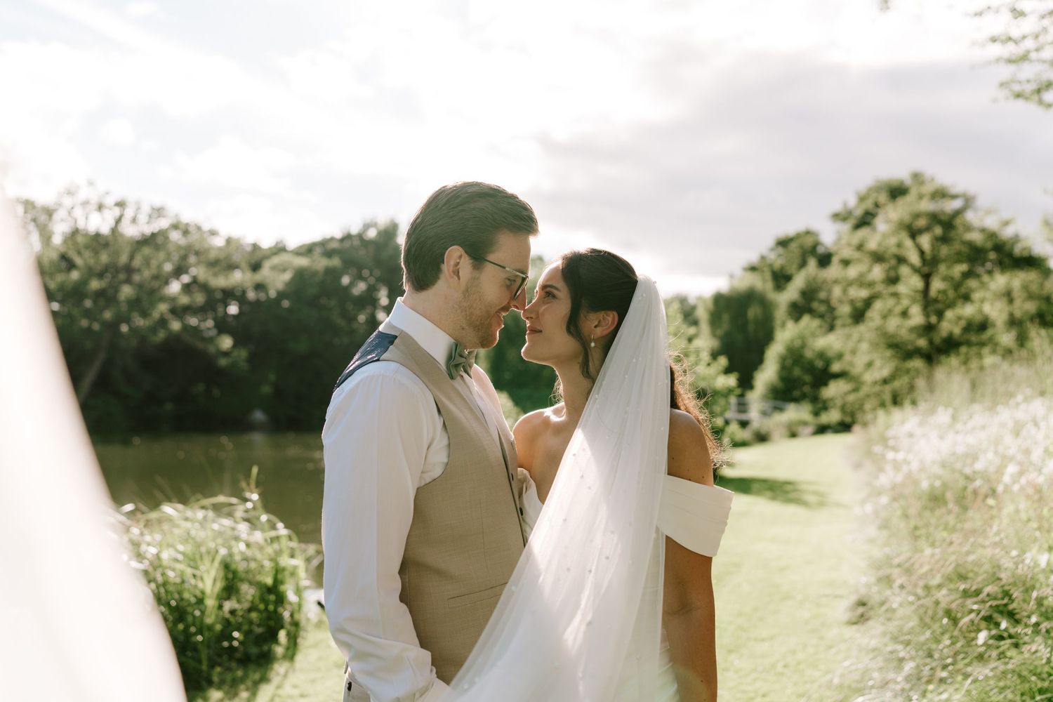 Bride and groom sharing a romantic moment outdoors with golden sunlight and a scenic garden backdrop on their wedding day.