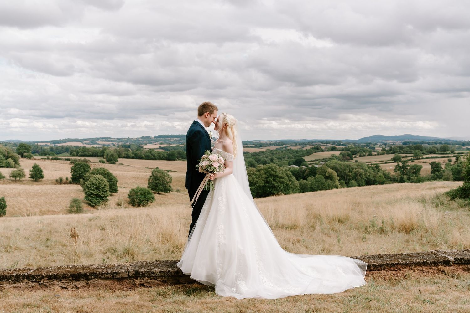 Bride and groom share a romantic moment overlooking rolling English countryside on their wedding day.