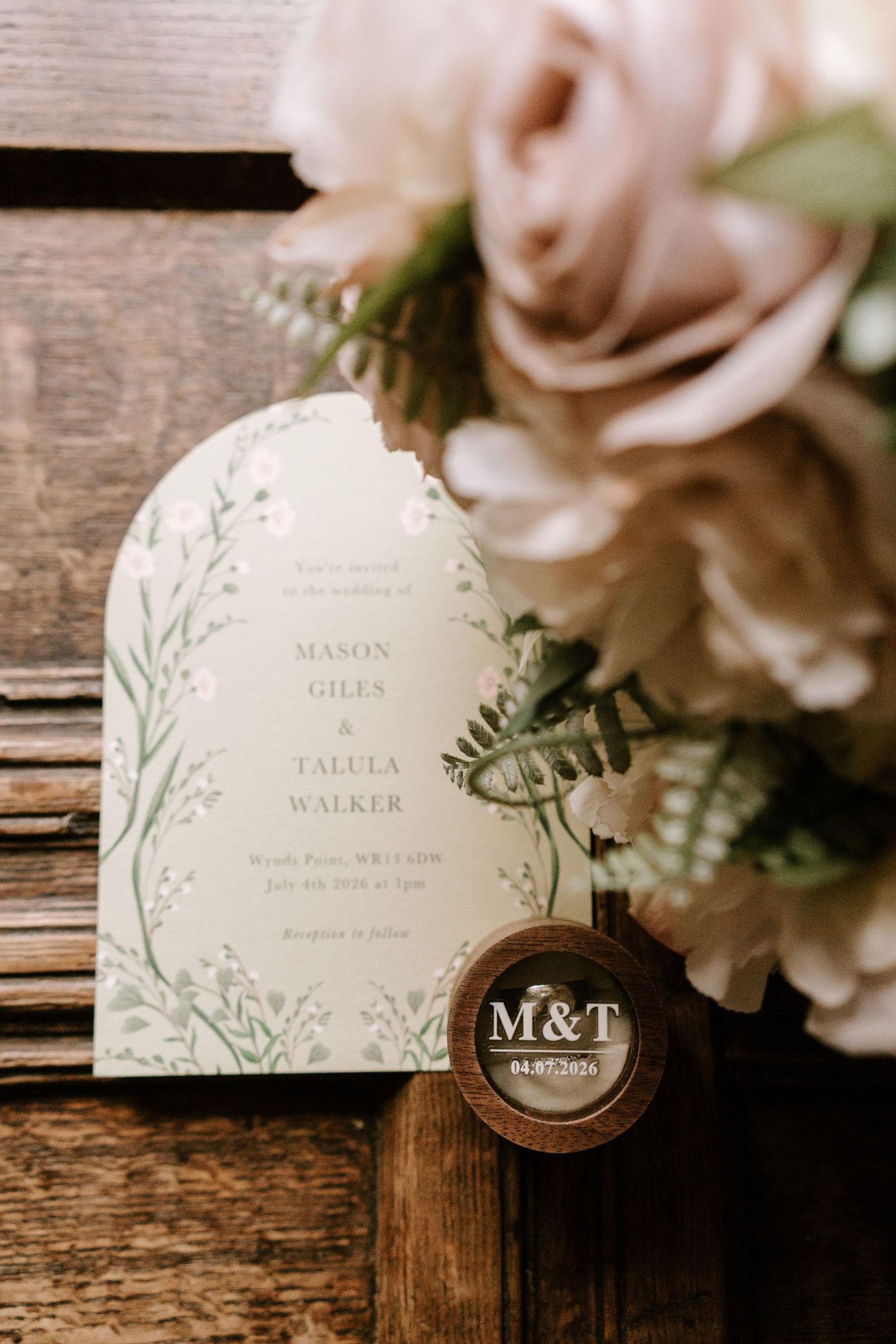 Elegant wedding invitation for Mason Giles and Talula Walker with floral greenery design beside a wooden ring box.