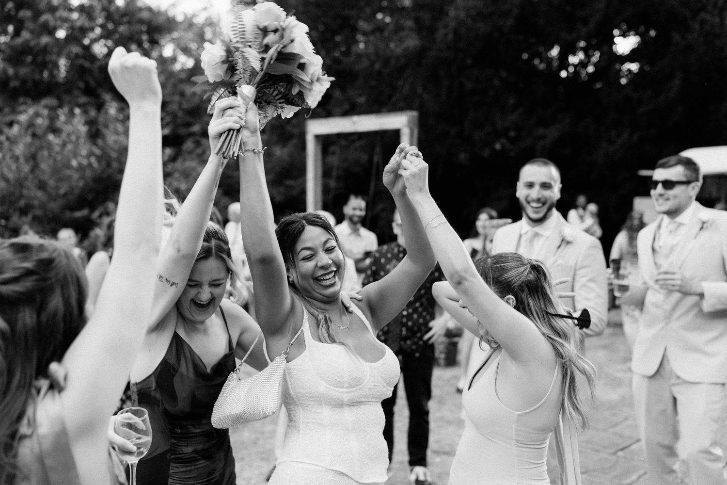 Bride joyfully celebrates with bridesmaids after catching the bouquet at an outdoor wedding reception.