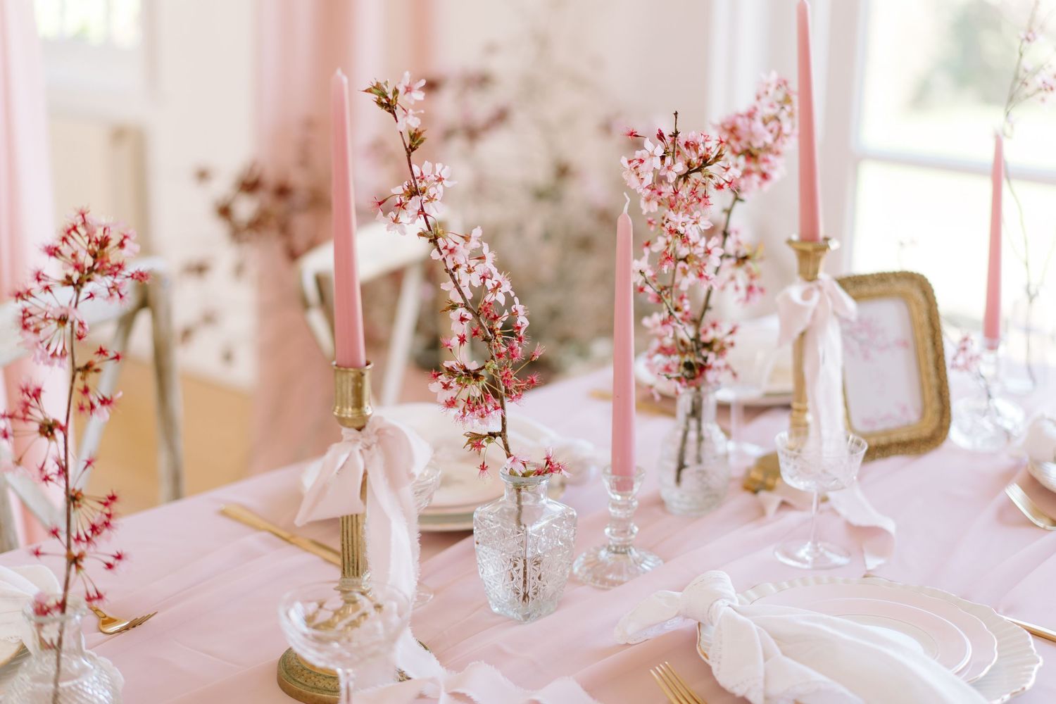 Elegant pink tablescape with cherry blossom branches, taper candles, and gold accents for a romantic spring wedding.
