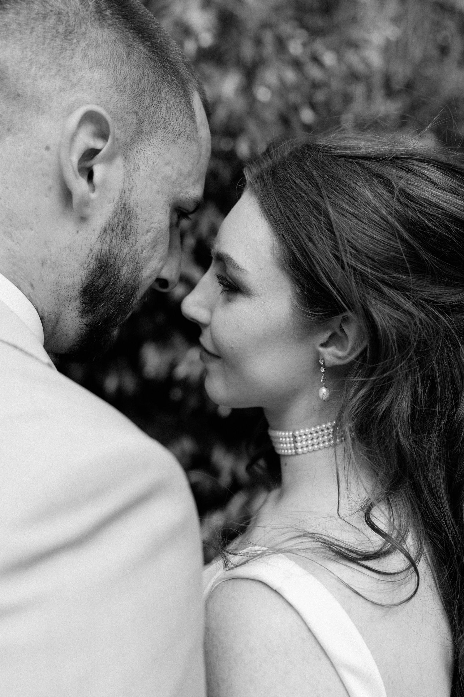 Black and white photo of a bride and groom sharing an intimate moment, foreheads close together outdoors.