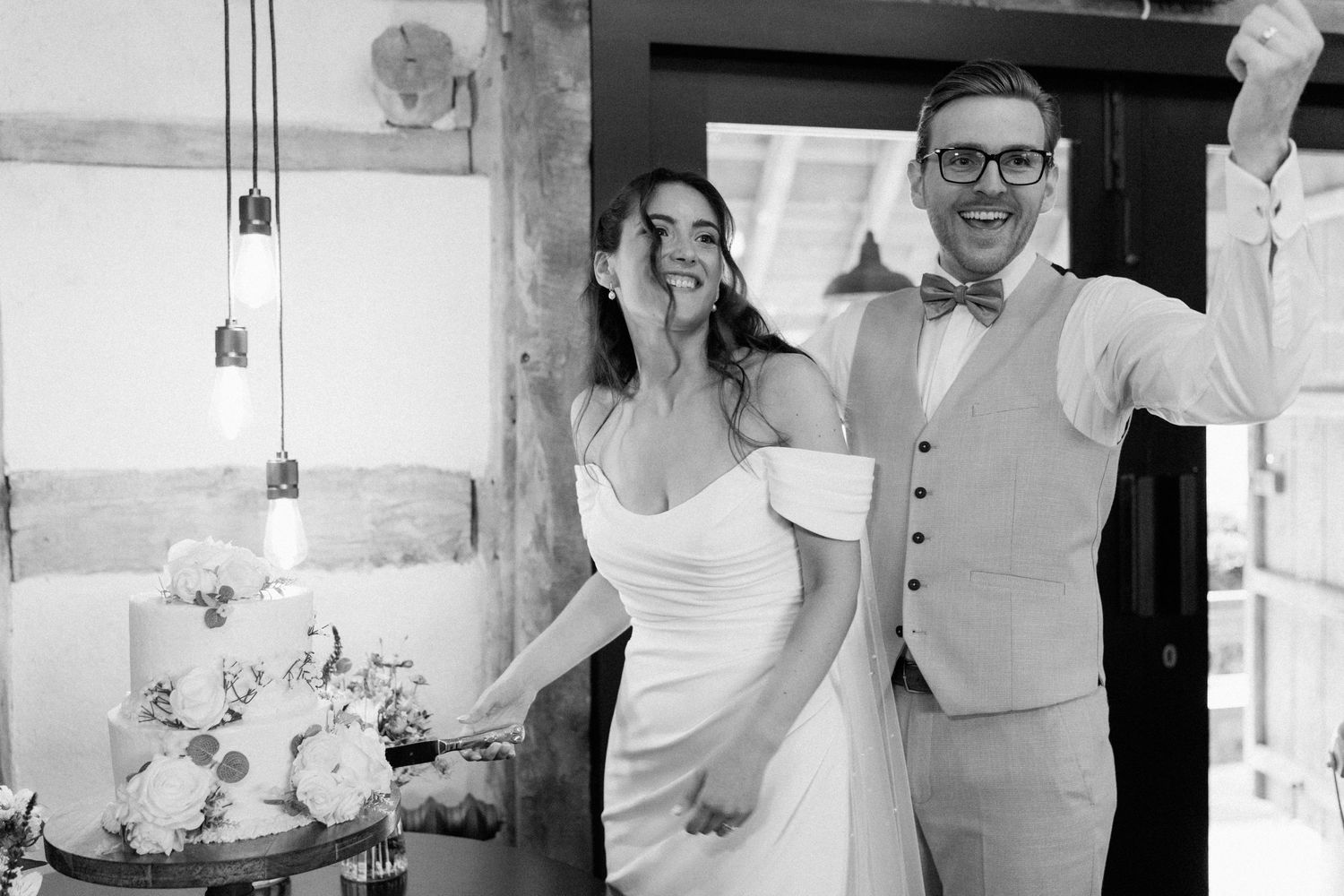 Black and white photo of smiling bride and groom celebrating near wedding cake.