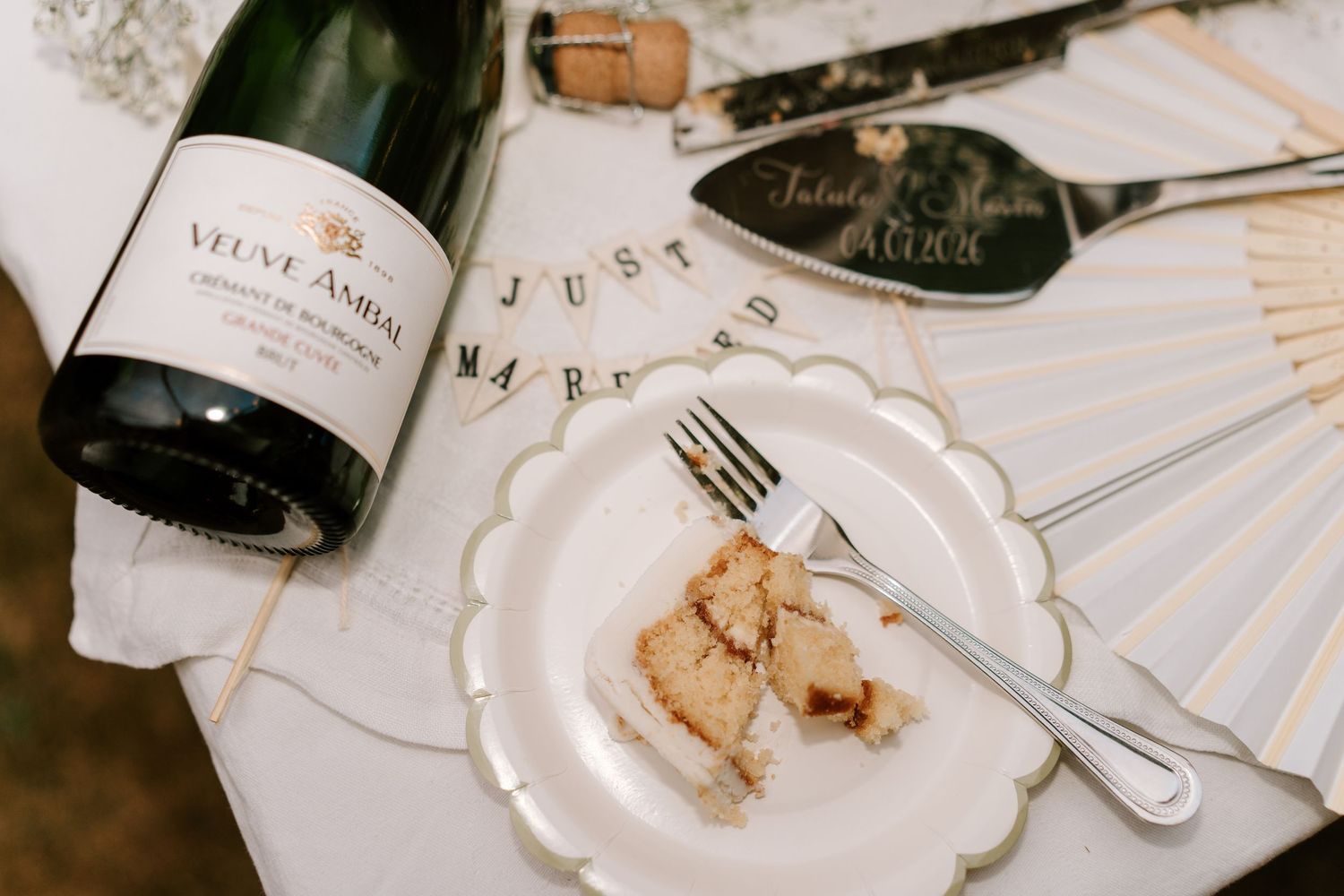 Wedding celebration flat lay with Veuve Ambal champagne, cake slice, and Just Married banner.