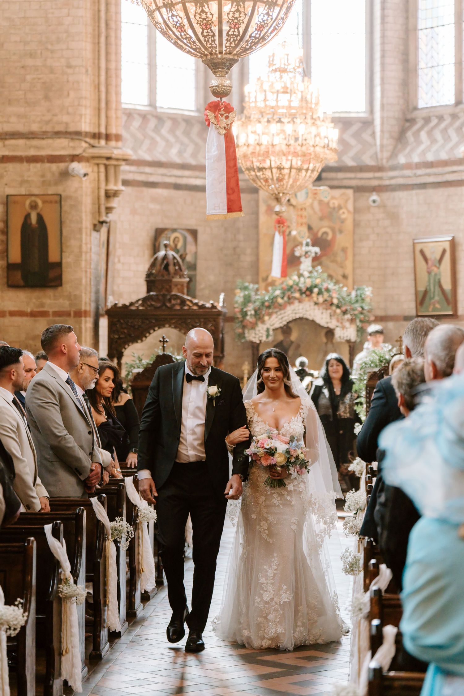 Bride and father walk down the aisle of an ornate church after their wedding ceremony.