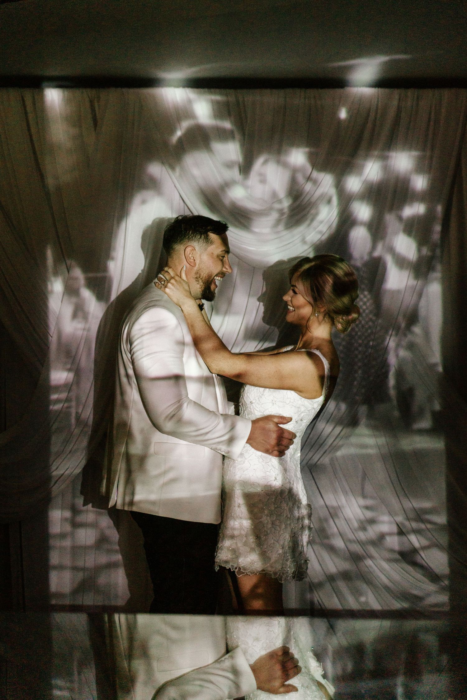 Bride and groom share romantic first dance, bathed in soft floral light projections at their elegant wedding reception.