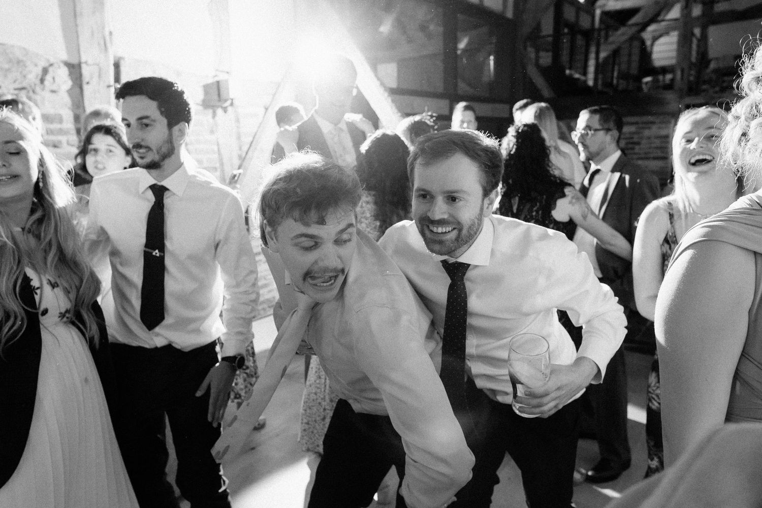 Black and white photo of guests dancing and laughing joyfully at a lively wedding reception celebration.